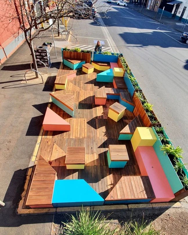 an outdoor seating area on the side of a road with wooden benches and planters