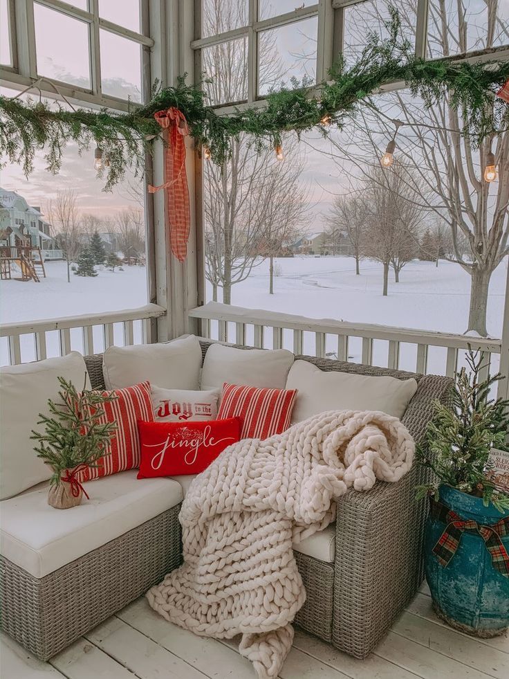 the porch is decorated for christmas with red and white throw pillows, greenery, and blankets