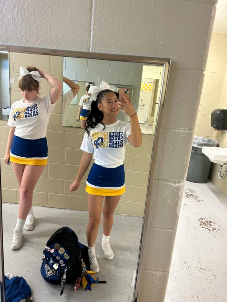 two girls in cheerleader outfits are reflected in a mirror