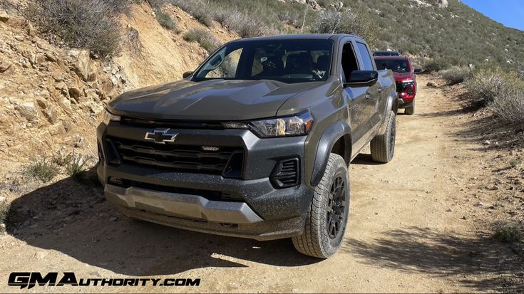 two pickup trucks driving down a dirt road