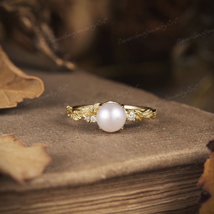 a white pearl ring sitting on top of a wooden table next to an oak leaf