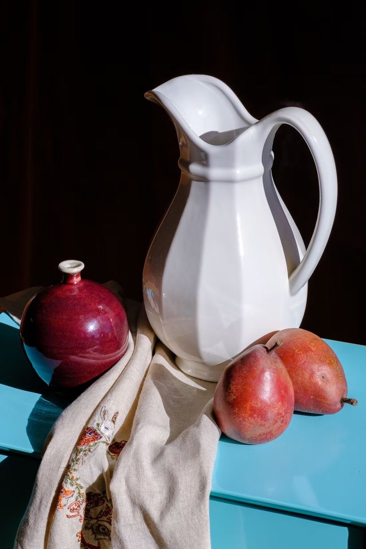 a white pitcher sitting on top of a blue table next to two pieces of fruit