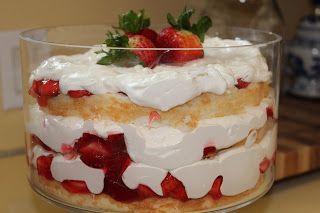 a layered cake with strawberries and whipped cream in a glass dish on a counter