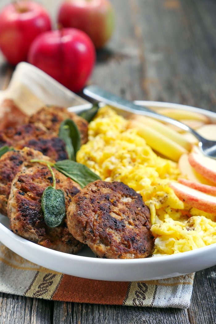 a plate with meat patties, scrambled eggs and fruit on it next to apples