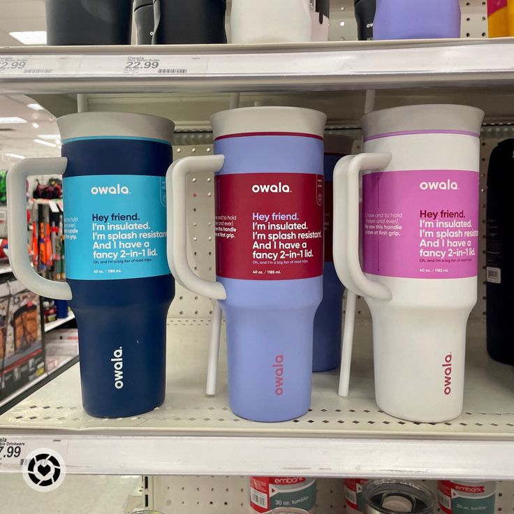 three travel mugs are on the shelf in a store, one is blue and one is pink