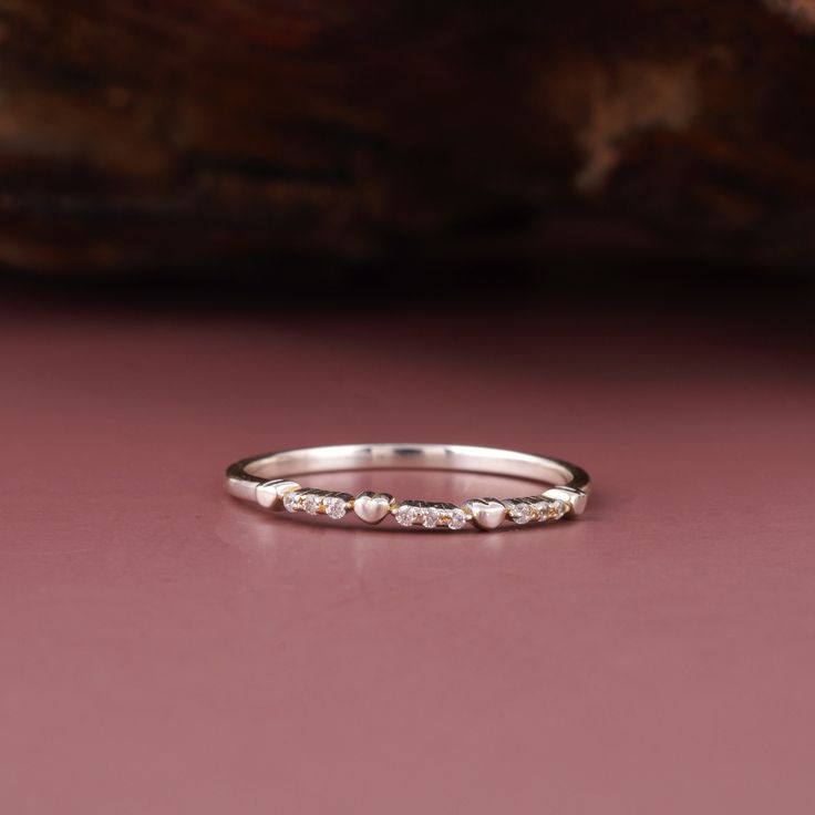 a white gold wedding band with five diamonds on the top and bottom, sitting on a pink surface