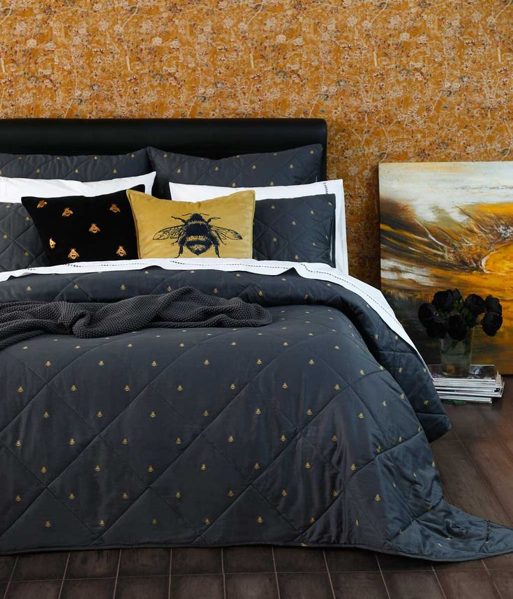 a bed with yellow and black pillows on it next to two framed pictures in front of a wall