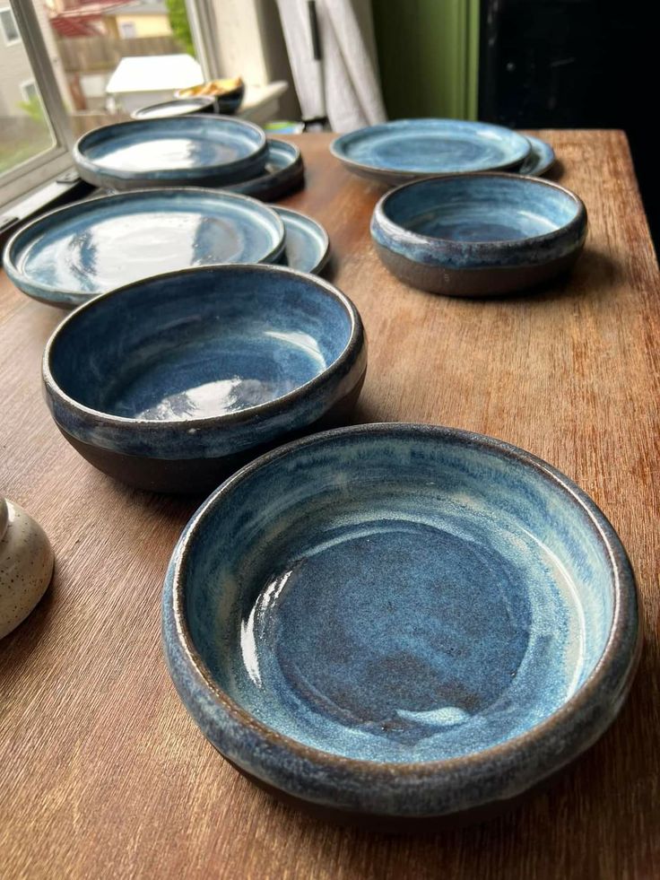 several blue bowls are lined up on a wooden table in front of an open window