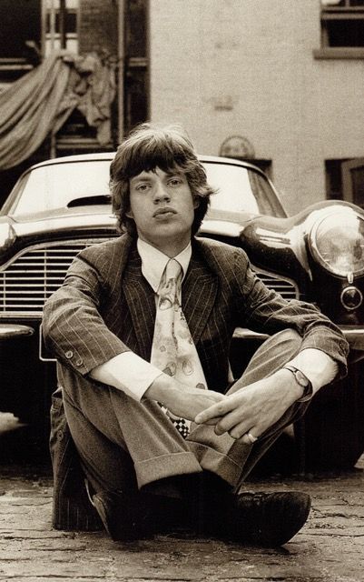 a man sitting on the ground in front of a car wearing a suit and tie