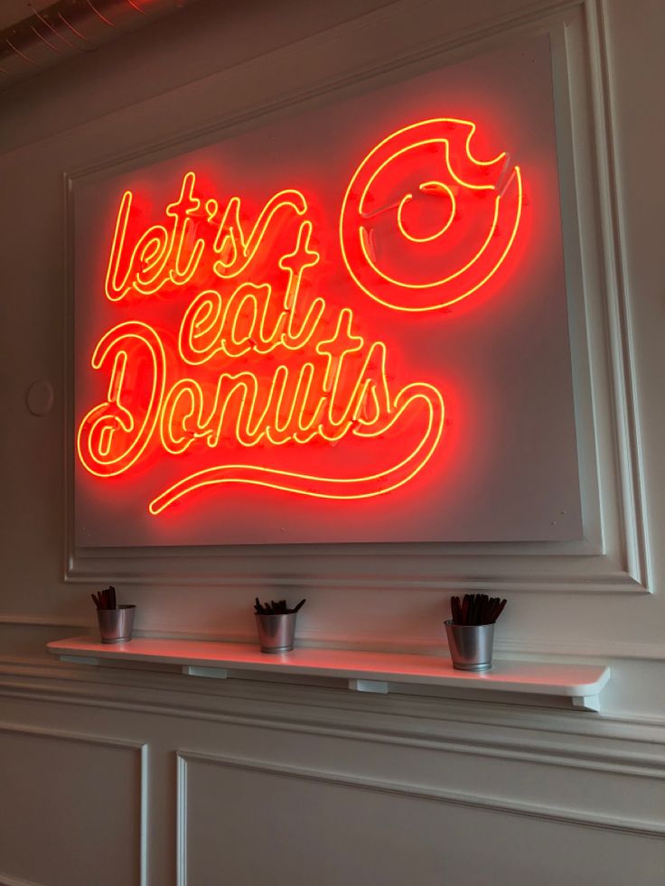 a neon sign that says let's eat doughnuts on the side of a wall