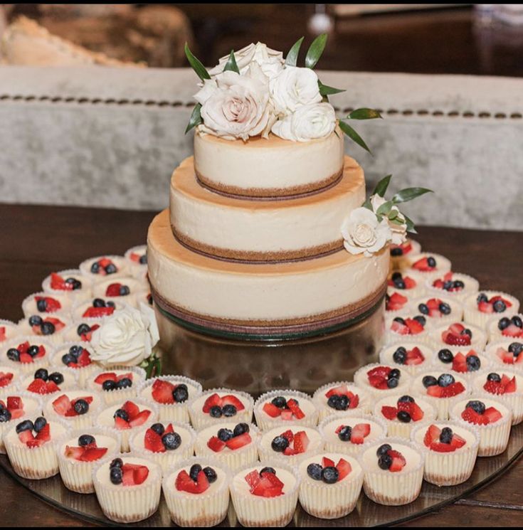 a wedding cake and cupcakes are arranged in the shape of a heart on a table