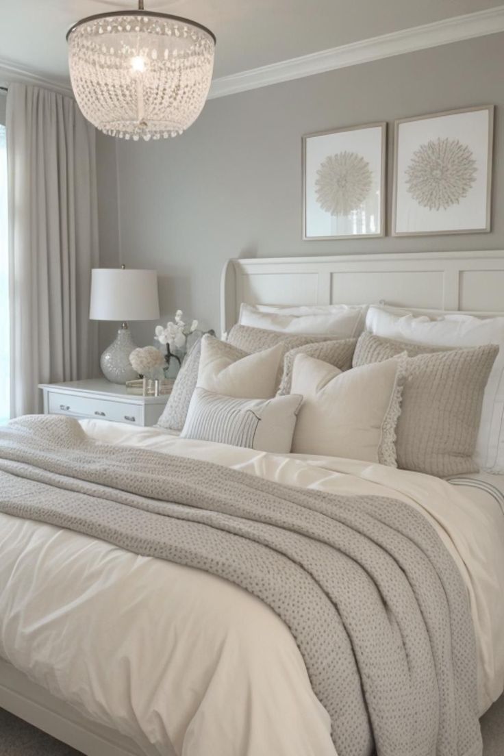 a white bed sitting under a chandelier next to a window in a bedroom