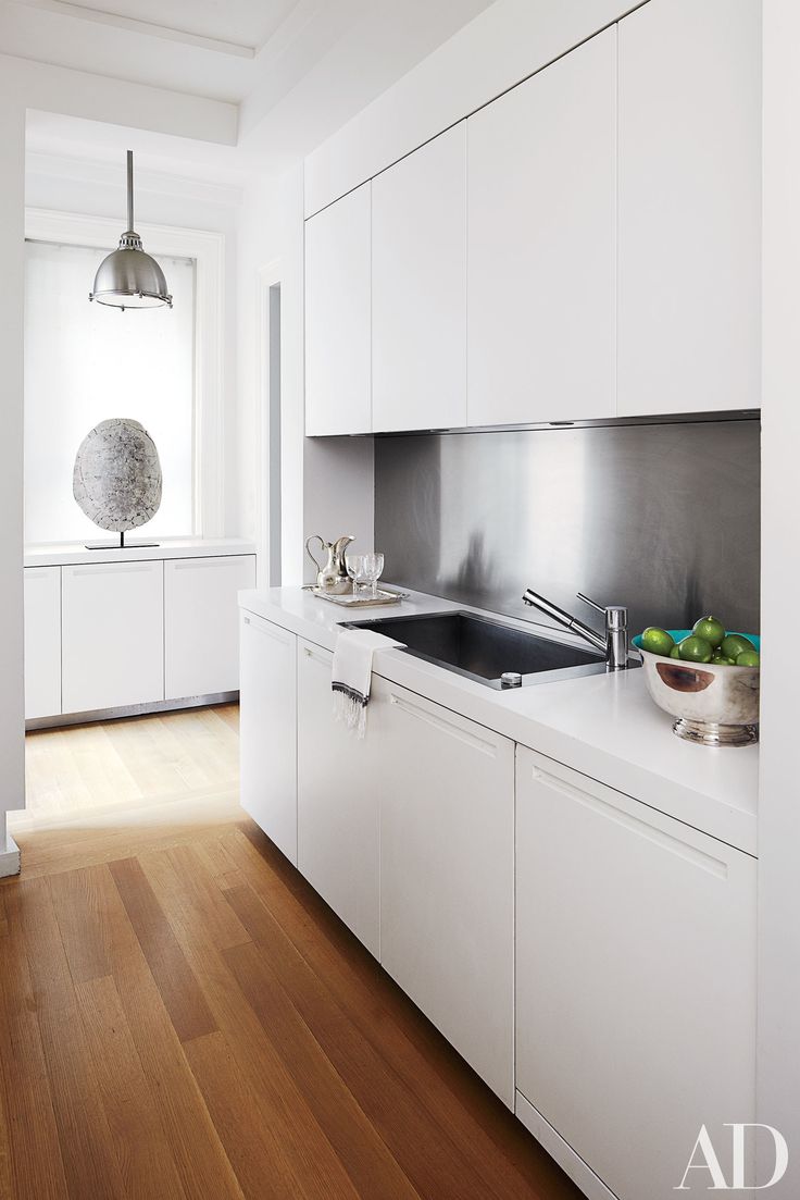 a white kitchen with stainless steel appliances and wood flooring, along with a bowl of fruit on the counter