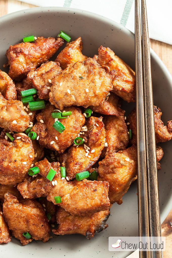 a bowl filled with chicken and chopsticks on top of a wooden table next to a napkin