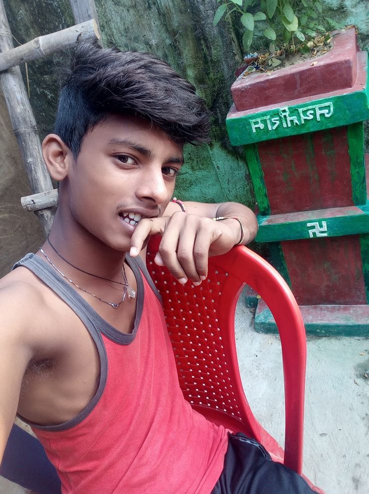 a young man sitting on top of a red chair next to a green planter