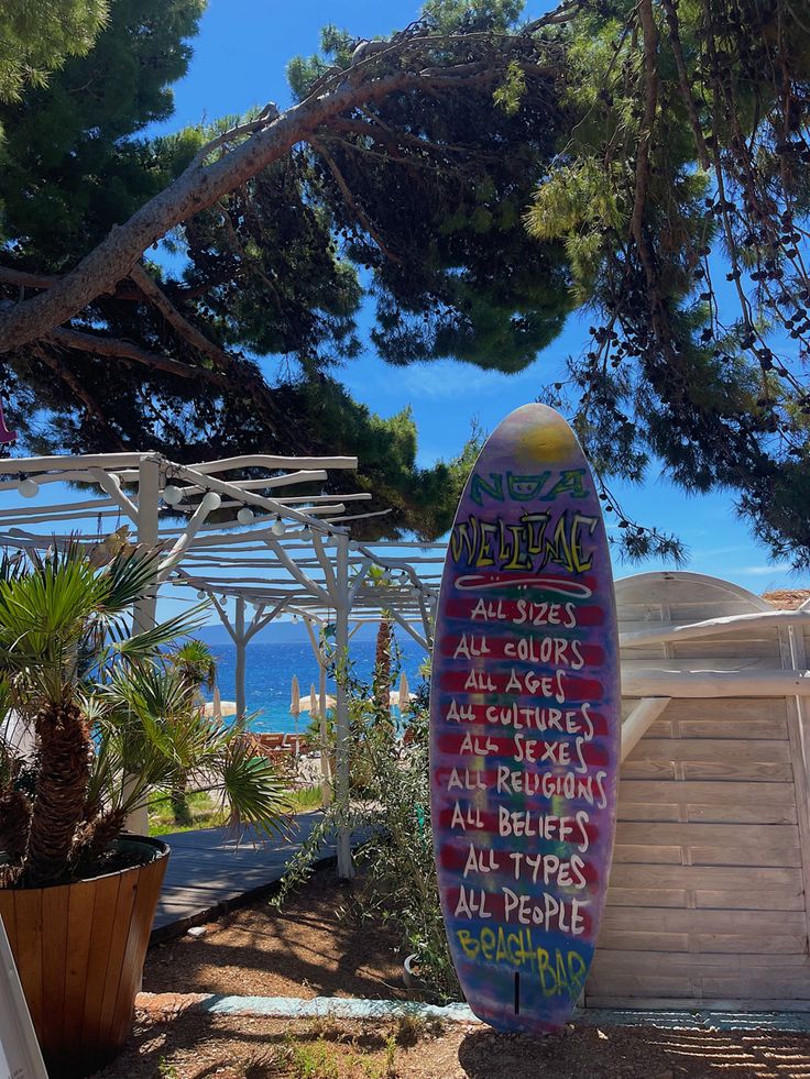 a surfboard with writing on it sitting in front of some trees