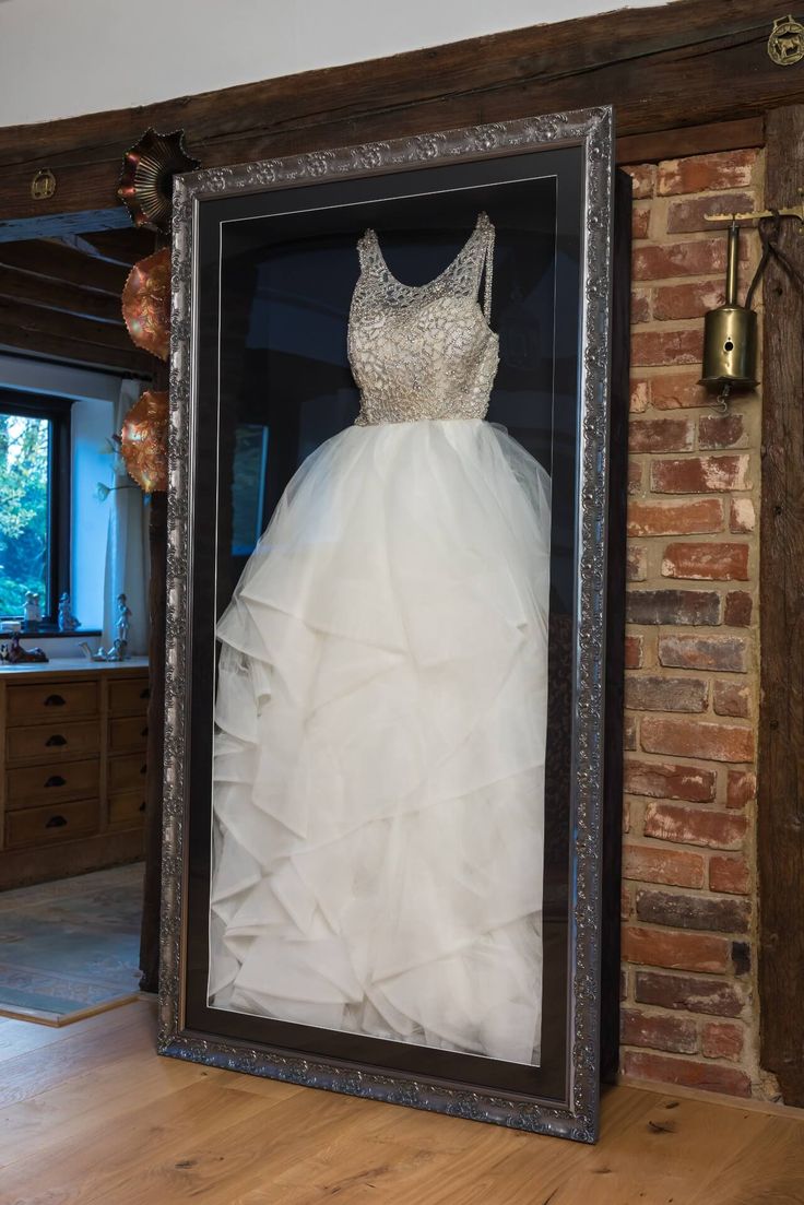 a wedding dress is displayed in a frame on the floor next to a brick wall