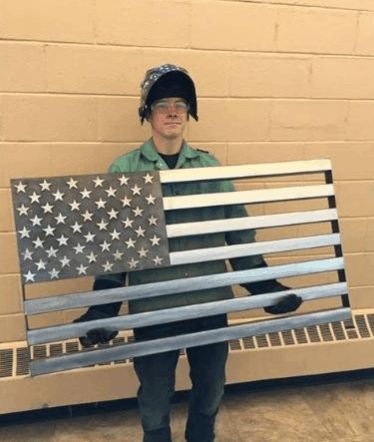 a man holding an american flag made out of metal bars and strips in front of a brick wall