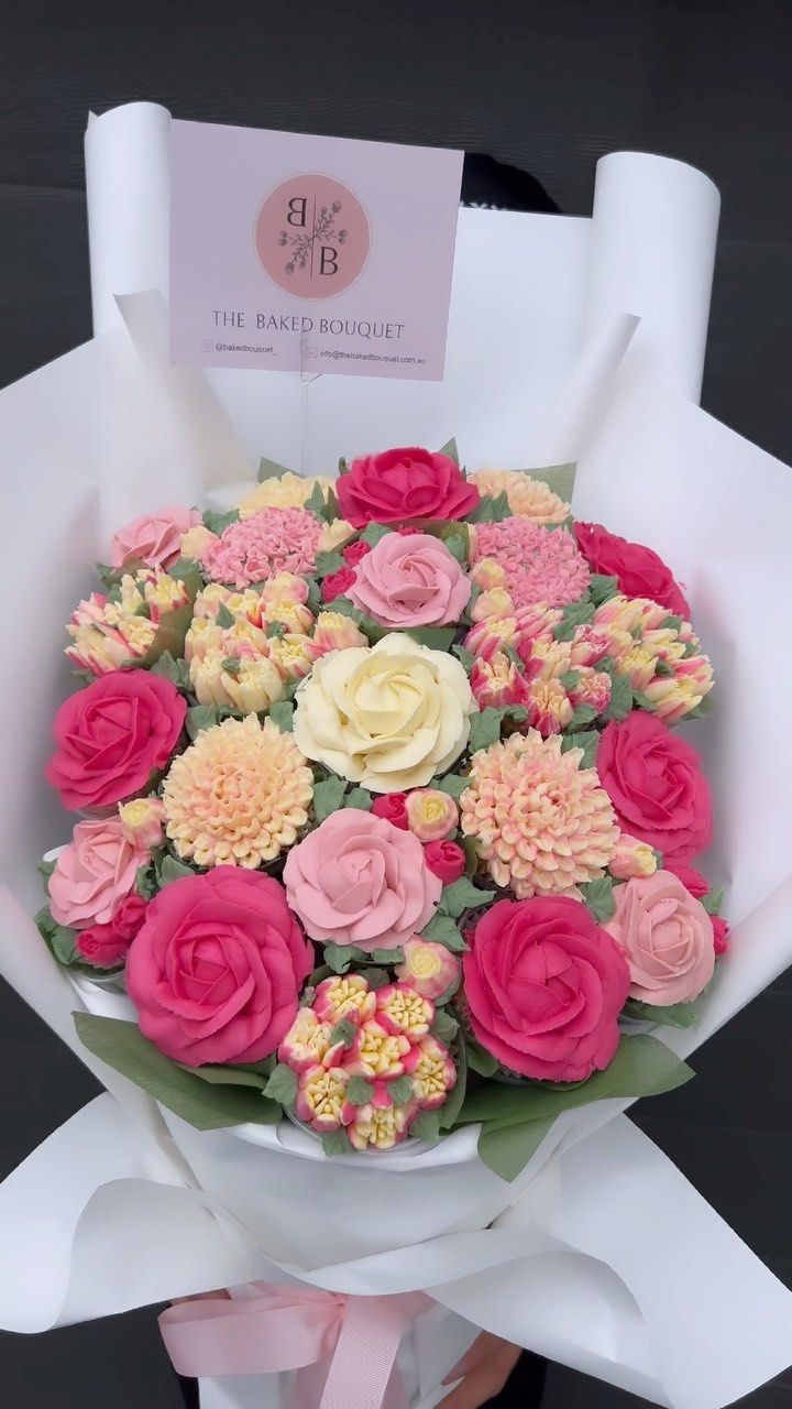 a bouquet of pink and yellow flowers is wrapped in white paper with a card on top