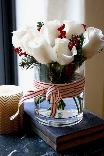 a glass vase filled with white roses sitting on top of a table next to a book