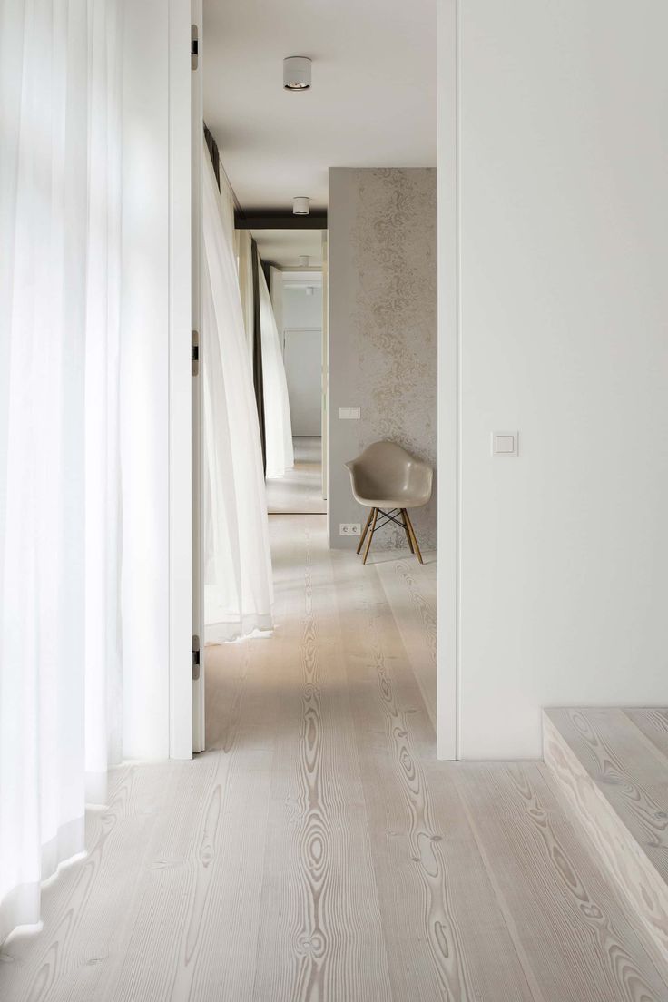 an open door leading to a white room with wood flooring and curtains on the windowsill