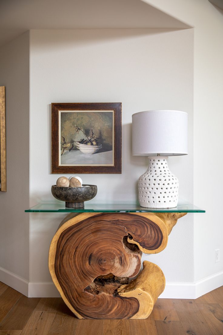 a wooden table with a glass top in a living room next to a painting on the wall