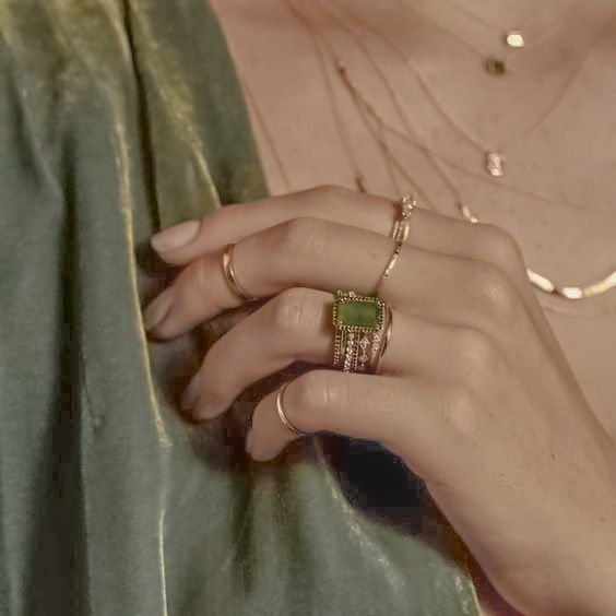 a close up of a person's hand with two rings on their fingers and an emerald ring