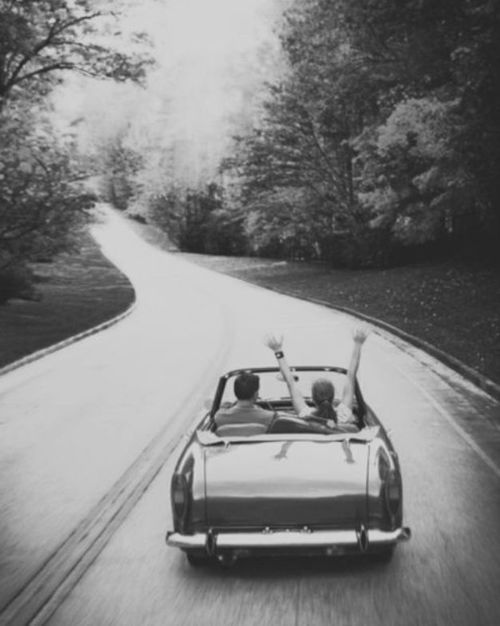 two people in a convertible car driving down the road