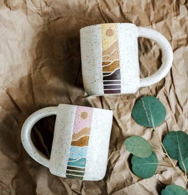 two coffee mugs sitting next to each other on top of a piece of paper