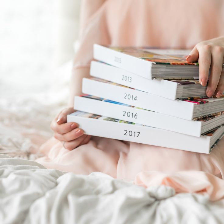 a person is holding three books in their hands while sitting on a bed with white sheets