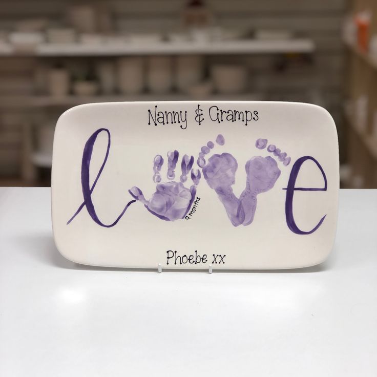 a white plate with purple handprints on the front and bottom that says, namny & grandpas love