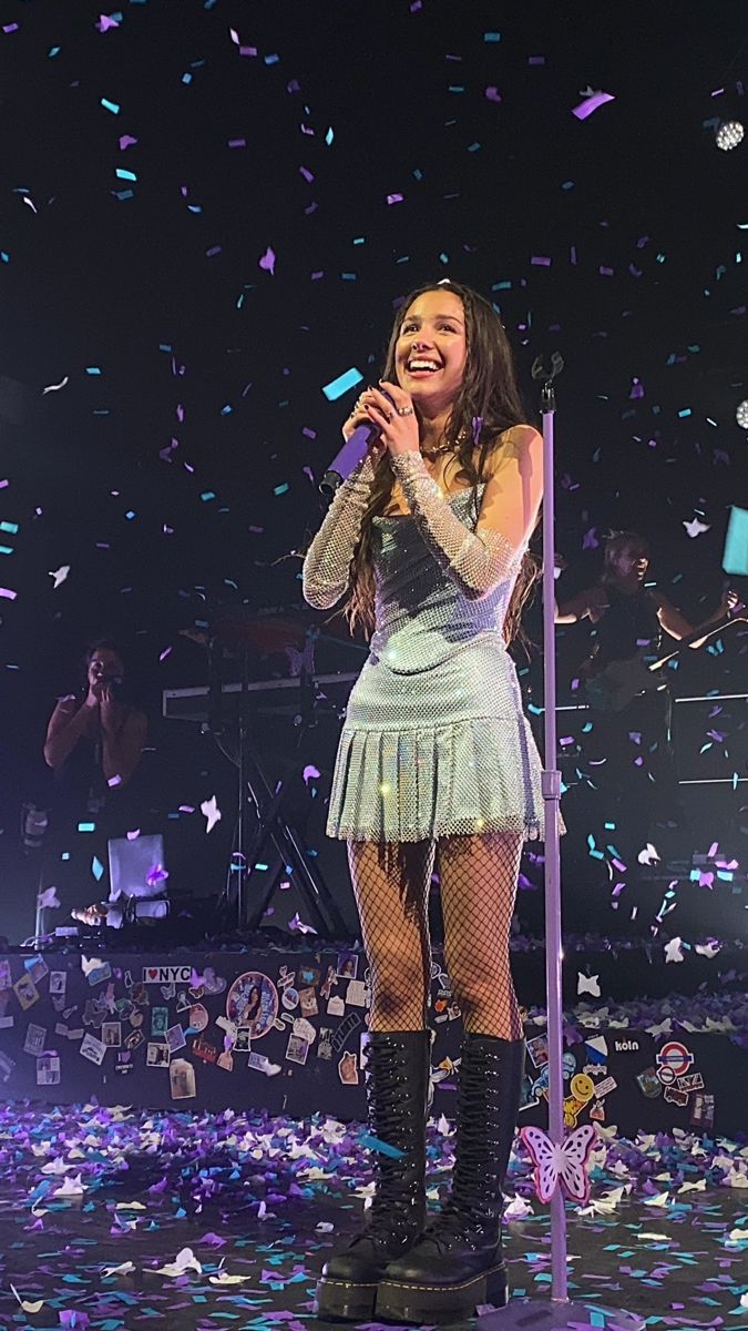 a woman singing into a microphone on stage with confetti in the air behind her