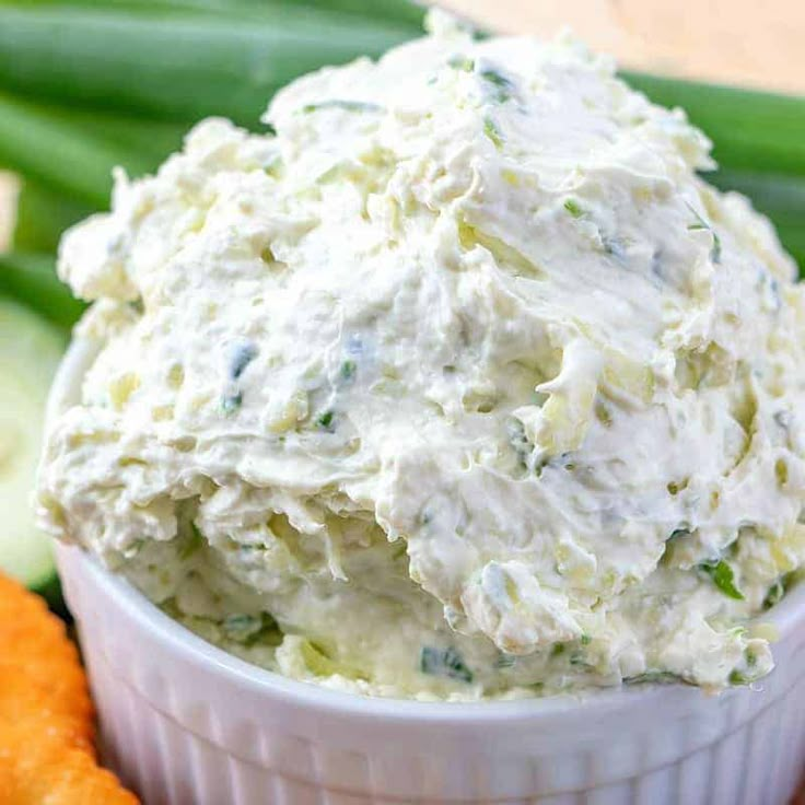 a white bowl filled with cucumber and cheese next to crackers on a table