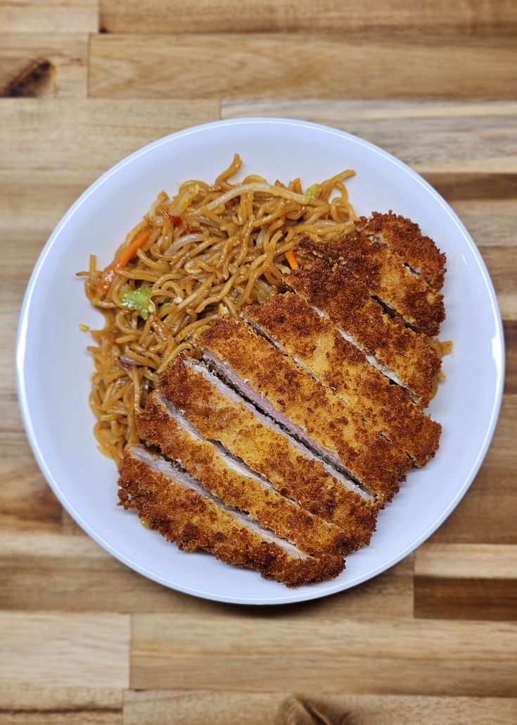 a white plate topped with meat and noodles on top of a wooden table next to chopsticks