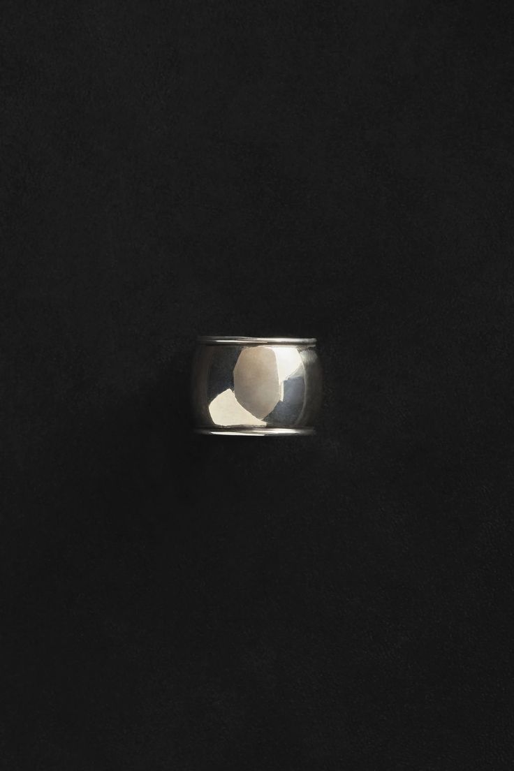 a silver ring on a black surface with the light reflecting off it's side