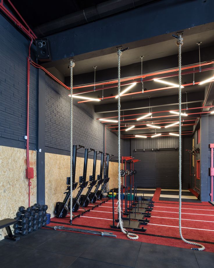 an indoor gym with rows of exercise equipment and ropes hanging from the ceiling, in front of a brick wall