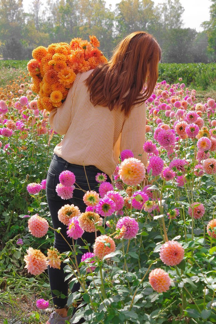 a woman with flowers in her hair is walking through a field full of pink and yellow flowers