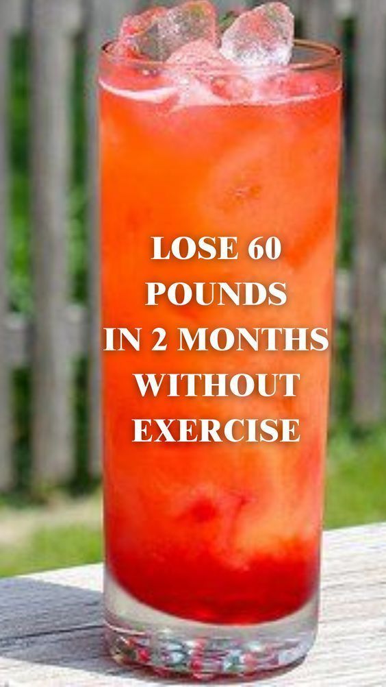 a tall glass filled with red liquid sitting on top of a wooden table next to a fence