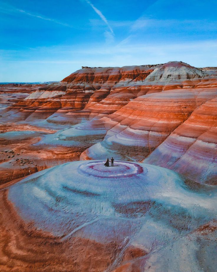 two people are standing in the middle of a vast area with red and blue hills