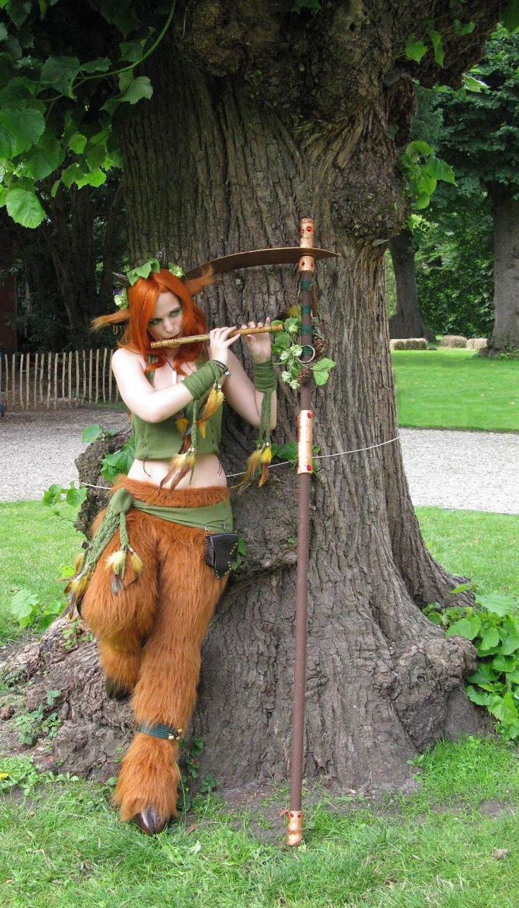 a woman dressed as a forest elf leaning against a tree