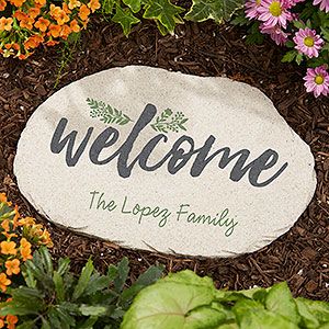 a welcome stone surrounded by flowers and plants