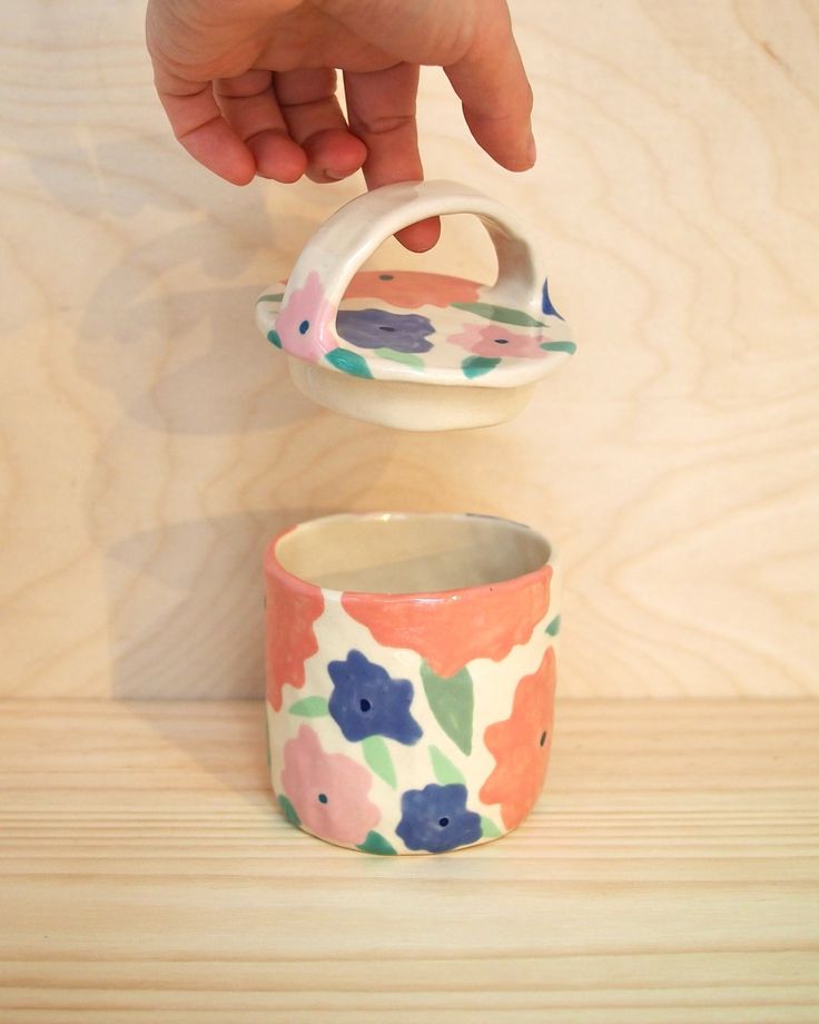 a hand is pouring something into a flowered cup on a wooden table with wood planks