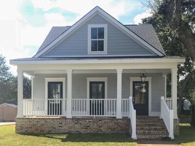 a small gray house with white porches and pillars on the front door is shown