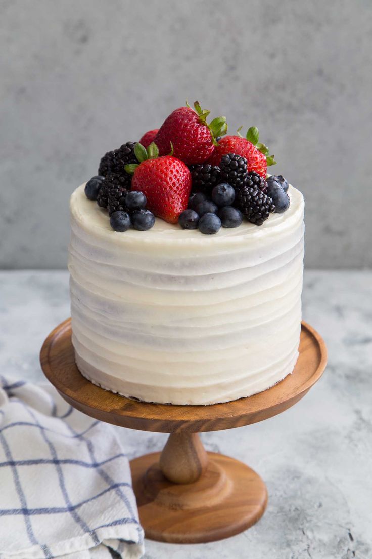 a white cake topped with berries and blueberries on top of a wooden platter