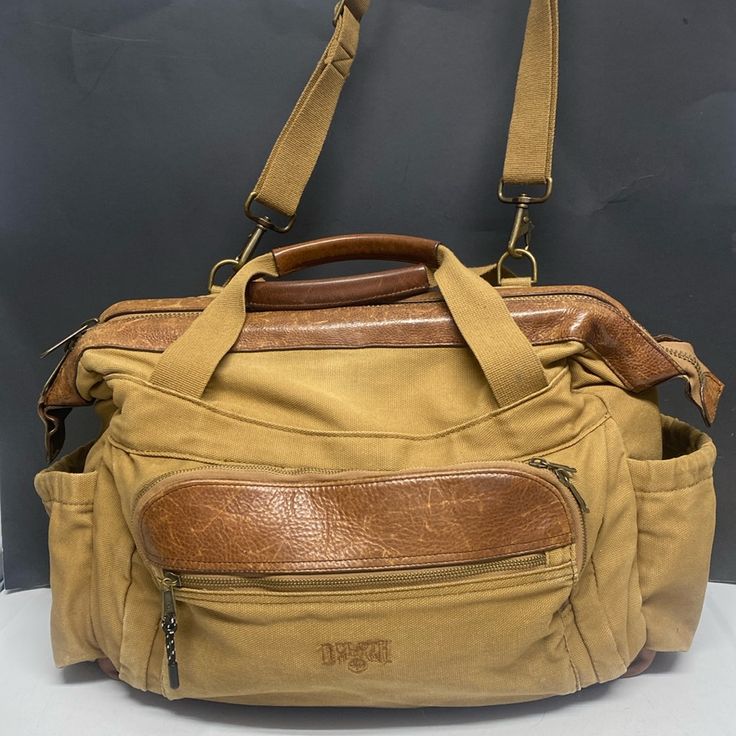 a tan leather bag with two straps hanging from it's shoulder and the bottom compartment open