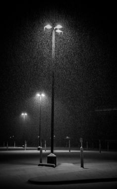 a black and white photo of a street light at night with snow falling on the ground