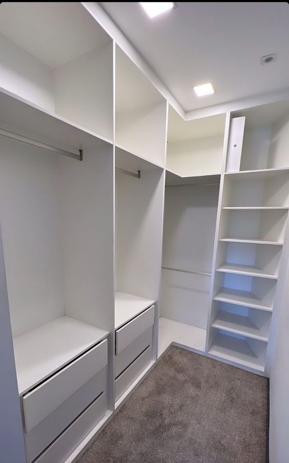 an empty walk in closet with white shelves and shelving units on the wall, along with carpeted flooring