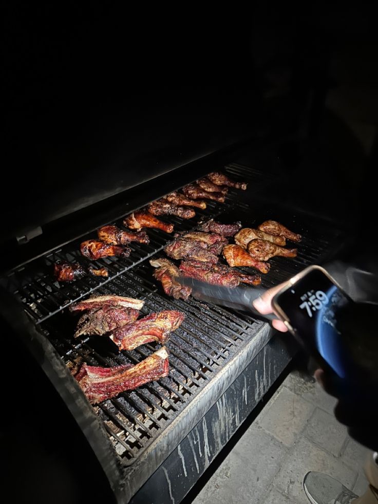 someone is grilling meat on the grill in the dark with their hand holding an object