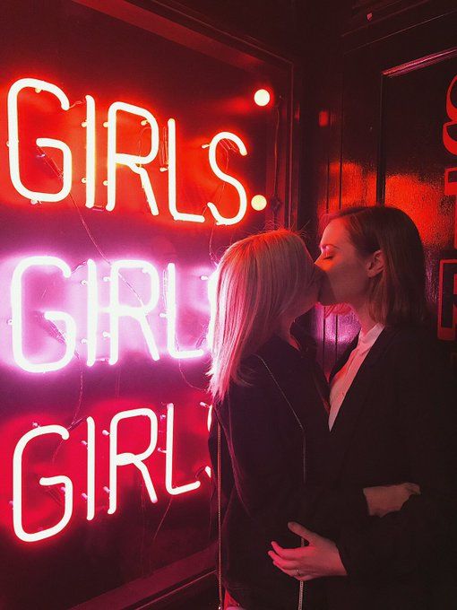 two women standing next to each other in front of a neon sign that says girls, girl