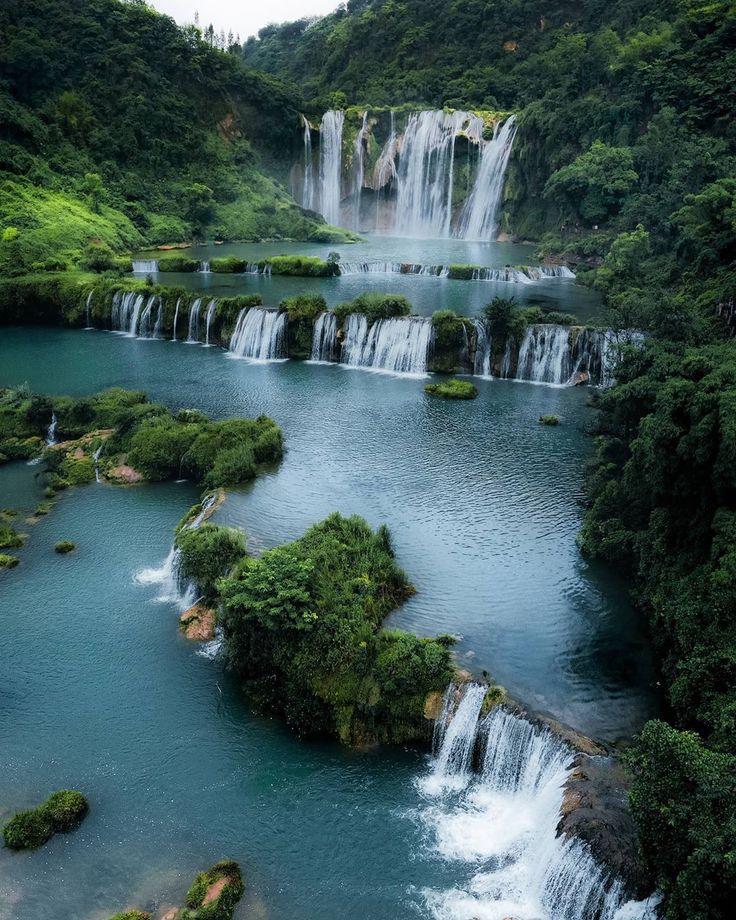 the waterfalls are surrounded by lush green trees and blue water in the foreground